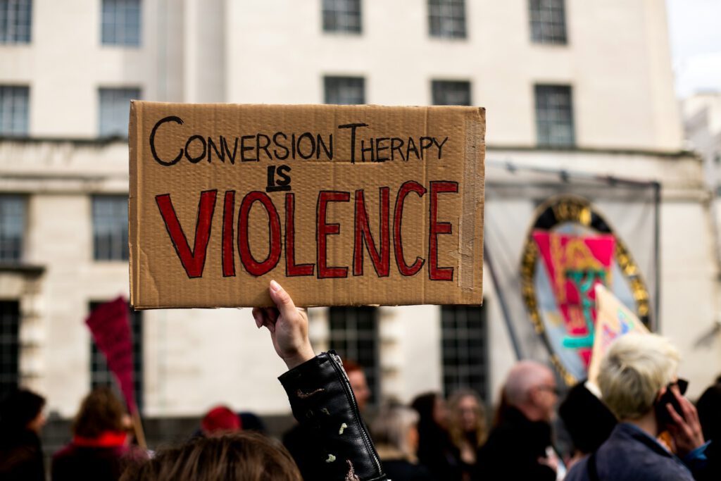 In einer Demo hält jemand ein Schild hoch, auf dem steht: Conversion Therapy is Violence