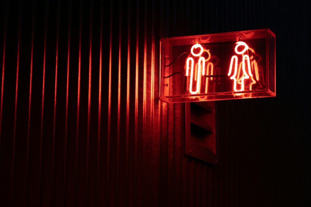 Rotes Neonlicht, Toiletten-Piktogramme für Mann und Frau, Symbolbild für Artikel "Mit Faktenfreiheit gegen Transfeindlichkeit und Rechtsextremismus"