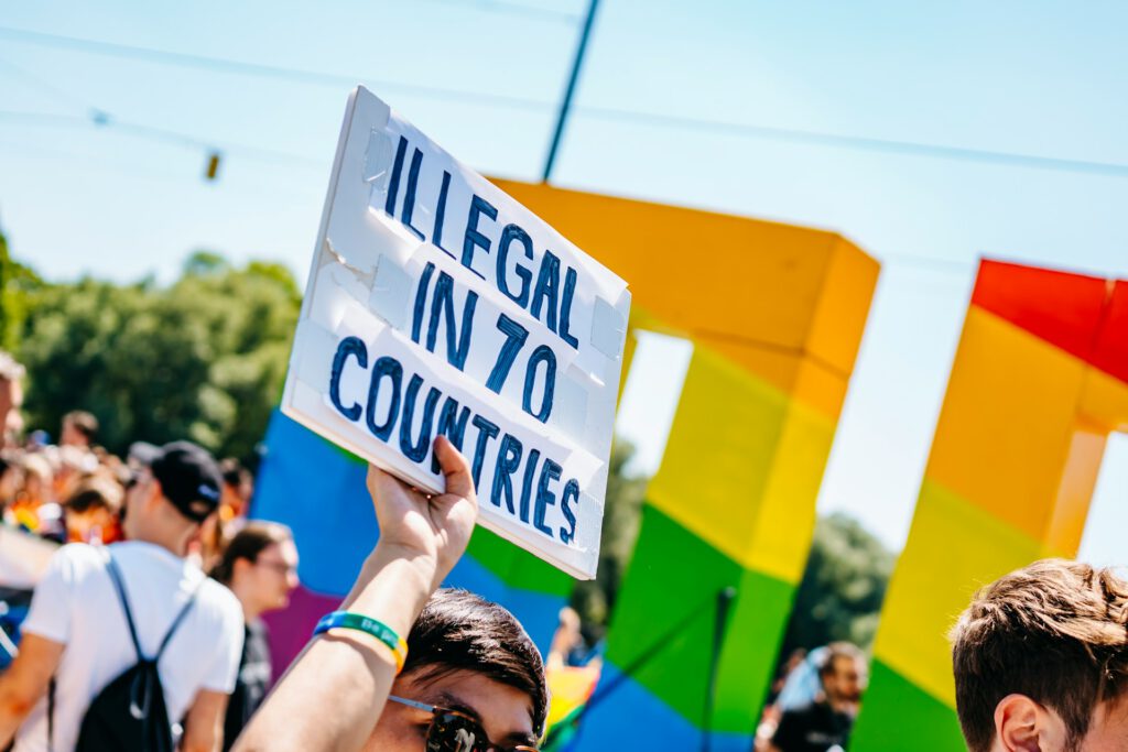 Ein Mann hält auf dem CSD München 2022 ein Schild mit der Aufschrift "Illegal in 70 Countries" hoch. Symbolbild für Artikel "Zum IDAHOBIT 2025: Paragraph 175 - Der lange Weg zur Rehabilitierung"