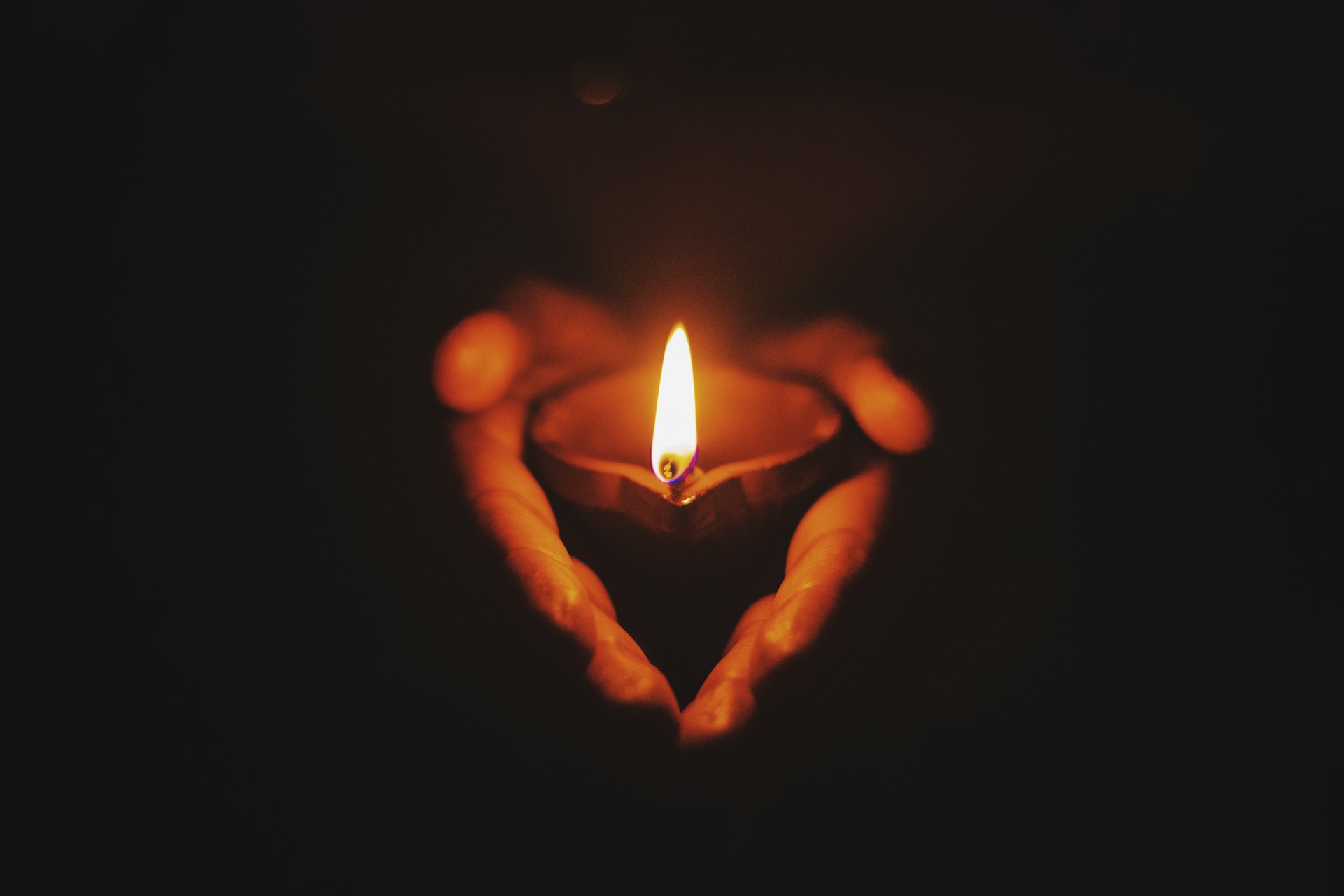 Ein angezündetes Teelicht wird in der Dunkelheit von zwei HÄnden gehalten. Symbolbild für Artikel "Transgender Day of Remembrance: Zwischen schamloser Übertreibung und Ignoranz".