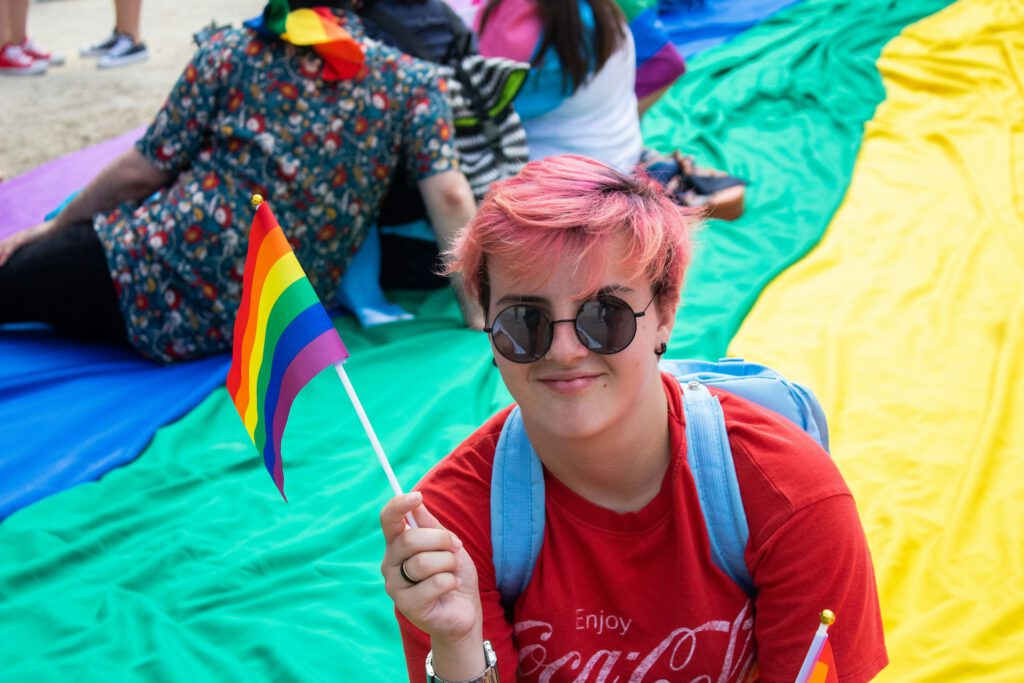 Eine junge queere Person hält eine Regenbogenflagge in der Hand