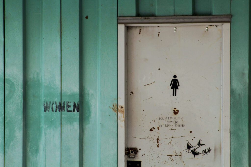 Eine Tür einer Toilette mit einem Symbol für Frauen. Daneben steht "Women". Symbolbild für Artikel „Geschlecht zählt“-Bericht: Wie Förderpolitik die Definition von Geschlecht in Deutschland verändert.